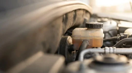 Vue en gros plan du réservoir de liquide de frein transparent sous le capot d'une voiture, montrant le niveau et la couleur ambrée du liquide